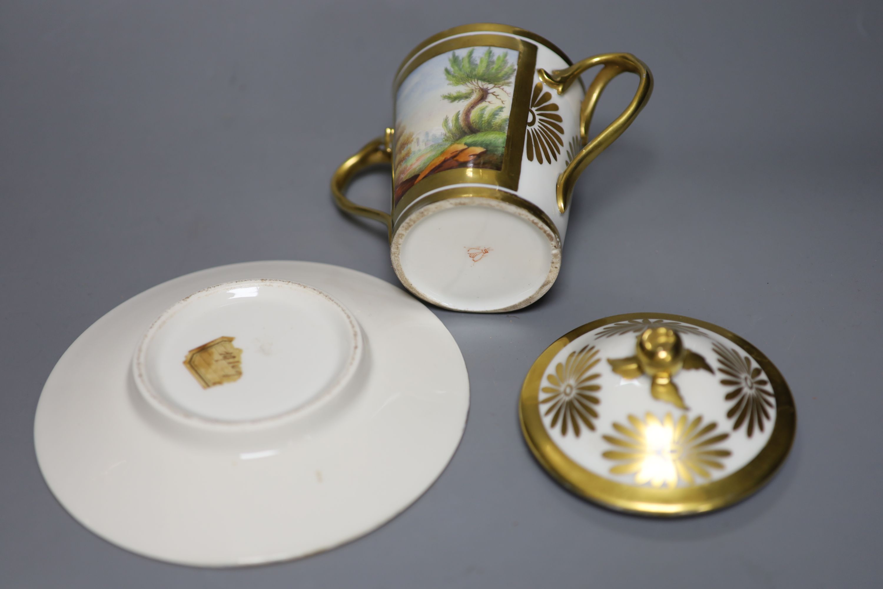 A 19th century Paris porcelain two handled chocolate cup, cover and stand painted with two landscapes in gilt panels to both the cup an